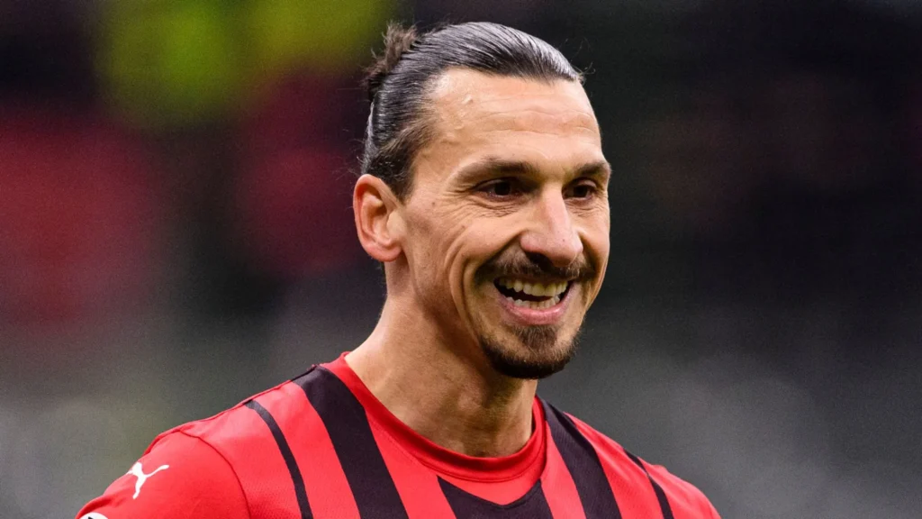 red t-shirt, smiling face , long hairs in a bun , moustache,XTB Inks Zlatan Ibrahimović as Their New Brand Ambassador